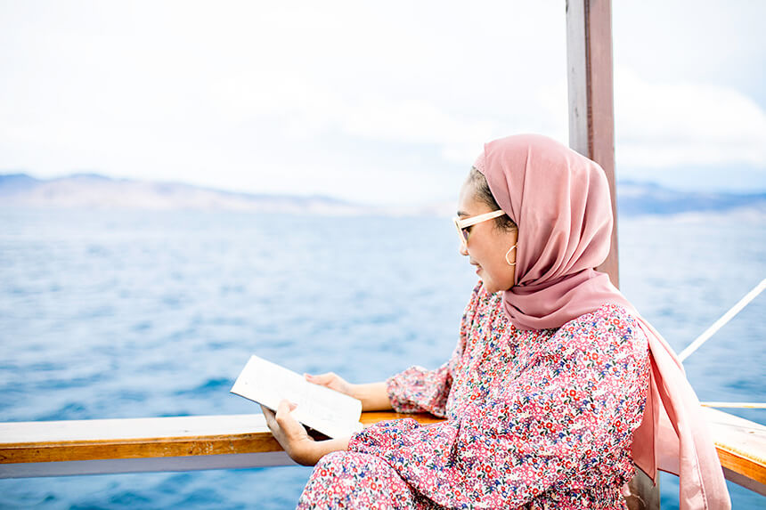 Donna musulmana asiatica seduta sul ponte a leggere un libro durante il viaggio in nave